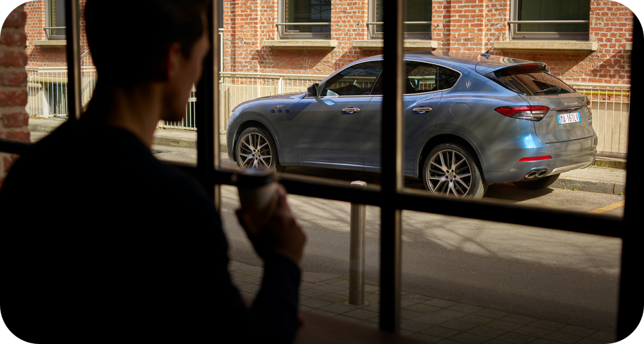 Mann mit Kaffeetasse schaut durch ein Fenster auf einen Maserati